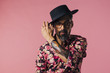  Portrait of a very cool mature artist with tattoo and glasses, touching his hat, isolated on pink studio background