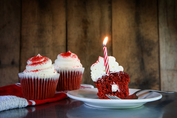 A red velvet cupcake with a candle on a wooden background