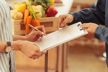 Wall Mural - Put your sign. Confident woman standing opposite deliveryman and checking document while receiving her order