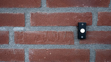 Background Of A Red Stone Wall With A Black With White Doorbell Button.