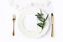Festive Table Summer Setting With Golden Cutlery, Olive Branch, Porcelain Dinner Plate And Silk Ribbon On White Table Background. Blank Card Mockup. Mediterranean Wedding Or Restaurant Menu Concept