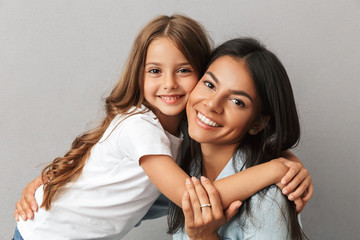 photo of attractive woman with little daughter smiling and hugging together, isolated over gray back