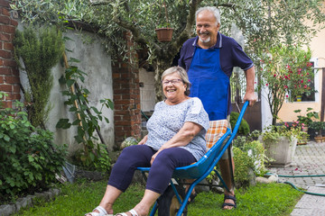 old man carry the aged wife at home outside in the jardin. laughing and happy together senior couple playing and joking at home. nice leisure activity outdoor for happiness lifestyle.