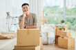 © DragonImages - Happy handsome ethnic man in casual clothes standing leaning on pile of large cardboard boxes for moving and looking at camera smiling with finger at cheek on blurred background of packed cartons and