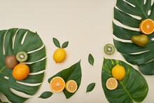 Top View Of Green Monstera Leaves With Composed Bright Ripe Fruit Of Pear And Kiwi And Citrus On Top