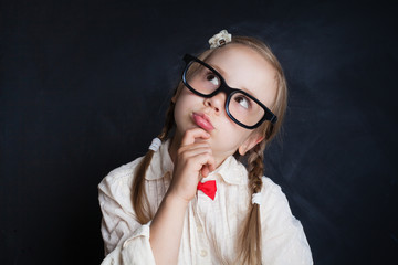 Happy smiling girl in glasses thinking and looking up on background with copy space. Back to school, Kid Creativity and Education Concept