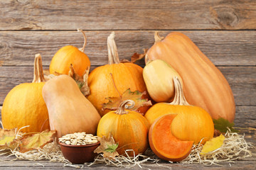 Wall Mural - Orange pumpkins with dry leafs and seeds on grey wooden table