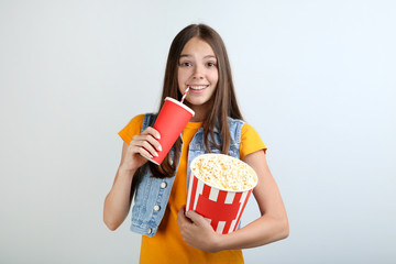 Young girl holding bucket with popcorn and paper cup on grey background