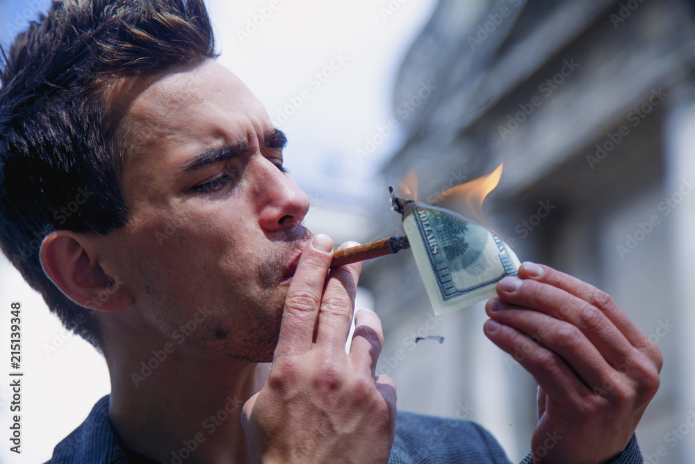 Young brutal businessman lighting cigar with $100 dollar bill Stock Photo