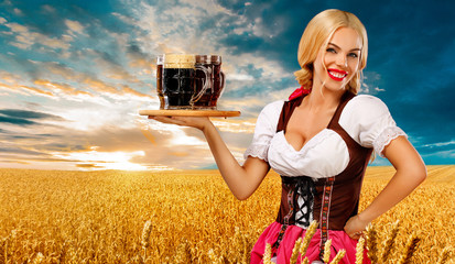 Wall Mural - Beer party. Sexy Oktoberfest woman - waitress, in Munich wearing a traditional german Bavarian dress, serving big beer mugs on golden wheat field background.