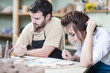 © danmorgan12 - Two Young Caucasian Ceramists Painting and Glazing Clay Crafts Together in Workshop with Paintbrushes.