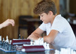 © Natali - cute handsome boy in white tshirt plays chess with his rival in chess class. Education concept, intellectual game. Chess tournament, lesson, camp, training concept