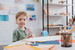 © LIGHTFIELD STUDIOS - portrait of preschooler boy sitting at table with paper and colorful pencils for drawing in classroom