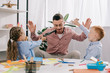© LIGHTFIELD STUDIOS - teacher in eyeglasses with hands up and kids with toy guns playing in classroom
