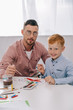 © LIGHTFIELD STUDIOS - portrait of teacher and little boy with paint brushes sitting at table in classroom