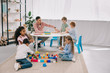 © LIGHTFIELD STUDIOS - teacher and multicultural preschoolers on floor with colorful bricks in classroom