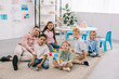 © LIGHTFIELD STUDIOS - smiling teacher and multicultural preschoolers sitting on floor with colorful bricks in classroom