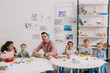 © LIGHTFIELD STUDIOS - smiling teacher and multiethnic kids sitting at table with colorful plasticine in classroom