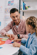 © LIGHTFIELD STUDIOS - smiling teacher and cute preschooler cutting papers with scissors att able in classroom