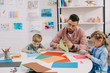 © LIGHTFIELD STUDIOS - portrait of focused teacher and preschoolers cutting colorful papers with scissors in classroom