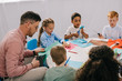 © LIGHTFIELD STUDIOS - partial view of male teacher and multiracial preschoolers cutting colorful papers with scissors at table in classroom