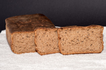 Black rye bread sliced on white material. Freshly baked homemade rye and white flour bread. Close up. Copy space.