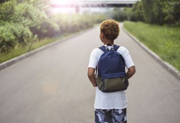 Portrait of the cute african american boy who is going to school with his school  backpack. Student mixed boy on his way to the school. Study for children. Road. Shooting on the july 2018. 