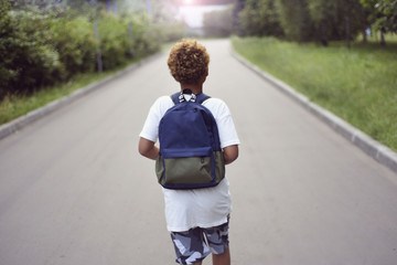 Portrait of the cute african american boy who is going to school with his school  backpack. Student mixed boy on his way to the school. Study for children. Road. Shooting on the july 2018. 