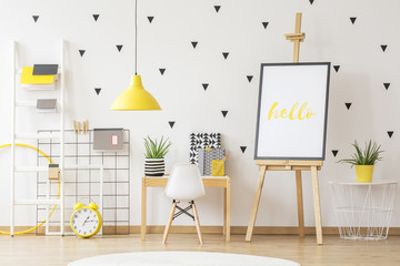 Wall Mural - Poster on easel next to wooden desk and white chair in child's room interior with yellow lamp. Real photo