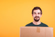 © DC Studio - Portrait of handsome young man holding a box in his hands. Delivery man on yellow background