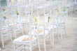 Side view of white chiavari chairs, wedding chairs arrangement for beach wedding venue on the white sand outdoors, White ribbin with rose flower flower deoration