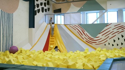 Wall Mural - Four young children of different ethnicities climbing stairs of inflatable structure in playroom and sliding down into cube pit