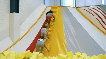 Wall Mural - Group of three multi ethnic children climbing stairs of inflatable structure in indoor playground when having fun together