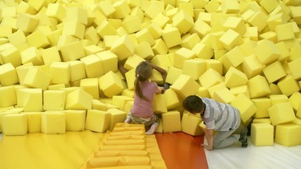 Wall Mural - Top view of three multi ethnic children playing together in cube pit in indoor amusement park, two of them helping the other