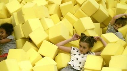 Wall Mural - Panning shot of four multi ethnic little children lying in giant cube pit when spending time together in indoor amusement park