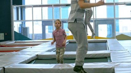Wall Mural - Tilt up shot of group of three little children jumping and bouncing on trampoline in indoor amusement park