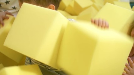 Wall Mural - Medium shot of group of playful little children having fun together in cube pit full of yellow soft foam cubes