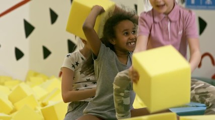 Wall Mural - Group of children of different ethnicities playing with yellow soft foam cubes in indoor playground