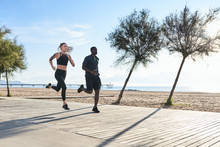 Side View Of Active Couple Running Along The Beach In Morning.