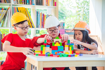 Three asian children wearing helmet and playing construction wood blocks at school library