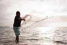 Fisherman Throwing Fishing Net On The Beach