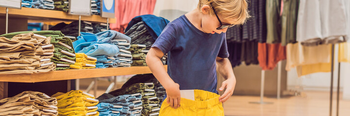 The boy tries on clothes in the childrens clothing store BANNER, long format