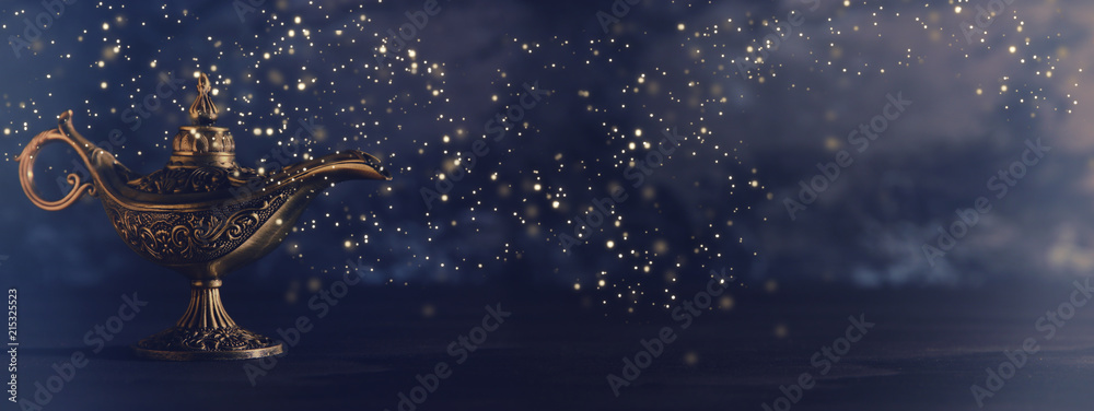 Image of magical mysterious aladdin lamp with glowing glitter lights over black background. Lamp of wishes. - obrazy, fototapety, plakaty 