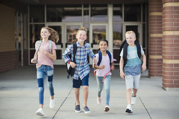 Wall Mural - Group of school kids running as they leave elementary school at the end of day. Going home from school happy and excited. Back to school photo