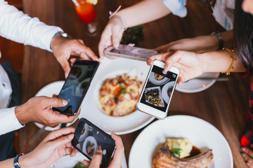 Group of friends going out and taking a photo of Italian food together with mobile phone.