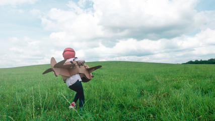 Cute little dreamer kid girl wearing pink helmet and aviator glasses flying in a cardboard airplane through the field, pretending to be a pilot