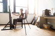 © proimagecontent - Tattoed amazing blonde curly girl in black hat drawing sketches behind the easel in studio near the sunny window