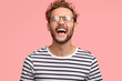 © WHstudio Leushin N - Overjoyed guy laughs joyfully as hears something funny, can`t stop happiness, has carefree lifestyle, wears spectacles, balck and white striped sweater, stands over pink background. Positive emotions