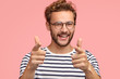 © wayhome.studio - Positive unshaven male points at you, has happy expression, curly hair, bristle, expresses his choice, wears striped clothes, isolated on pink background. Man does finger gun gesture. You are my type