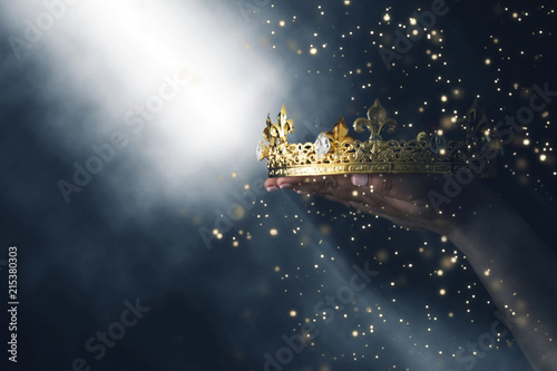 Fotografía mysteriousand magical image of woman's hand holding a gold crown over gothic black background